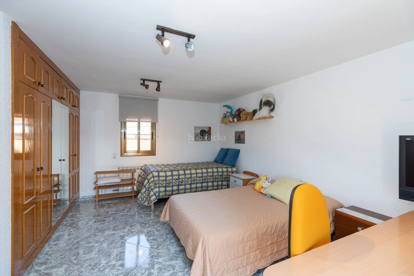 Dormitorio original con dos camas, armarios de madera y suelo gris. Fotografía con su marca de agua original.